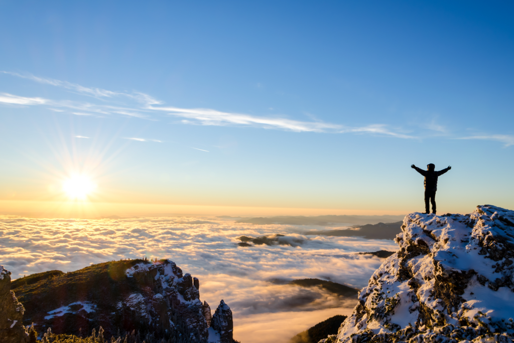 A hiker celebrates reaching the top of a mountain, looking over a mountain range