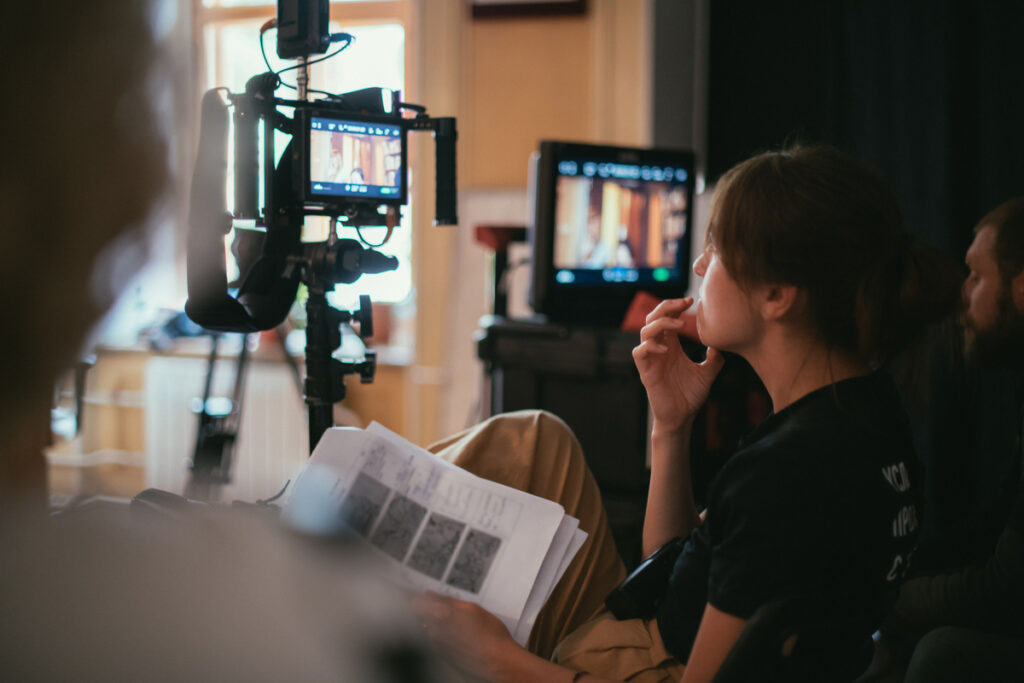 A director looks at screens on a film shoot while consulting her notes.